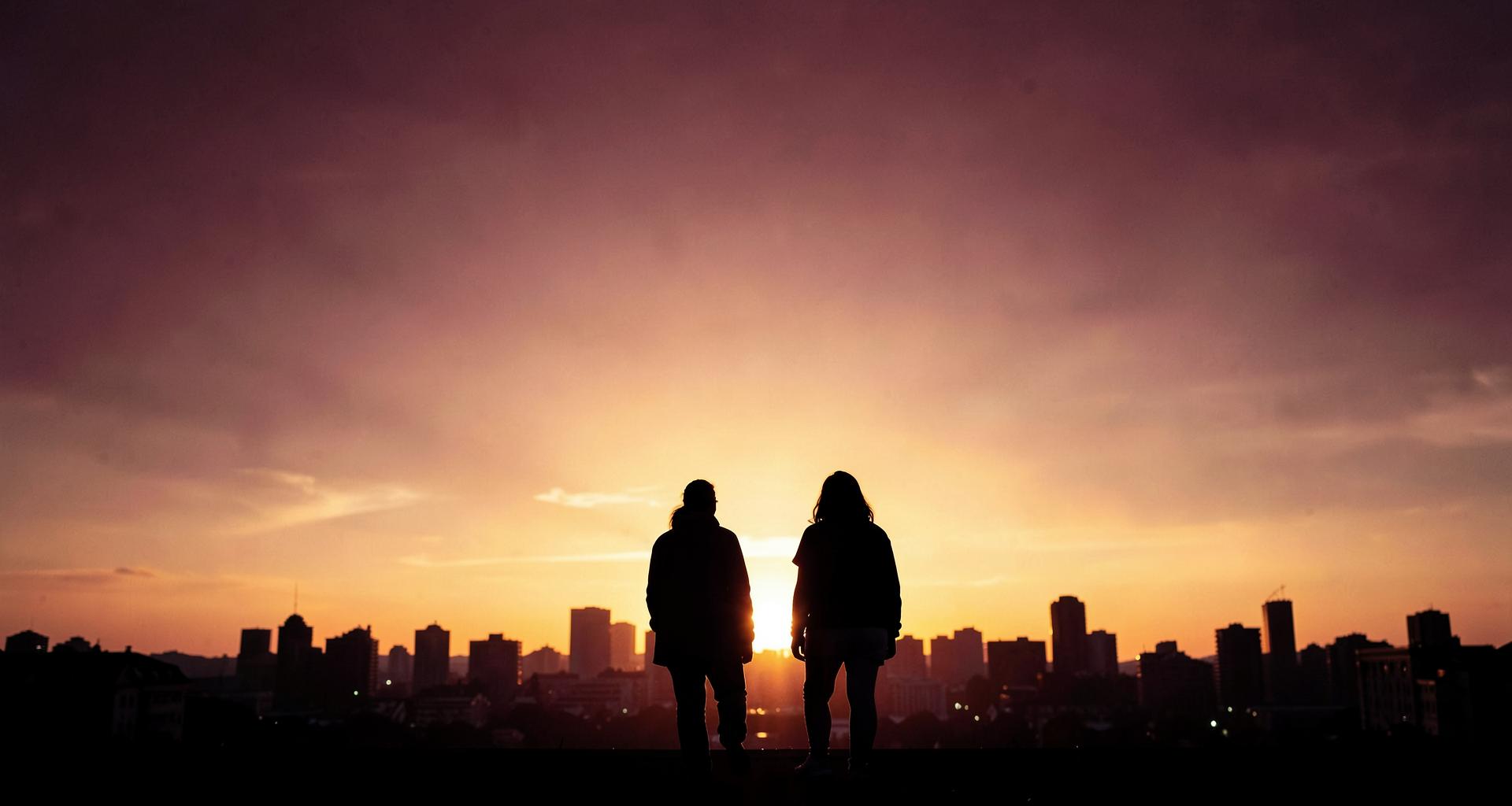 Two people standing side by side watching the sunrise over the city